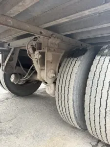 Dual rear axles of a refrigerated trailer showing tires and suspension components; visible are wheel hubs, leaf springs, brake lines, and frame members.