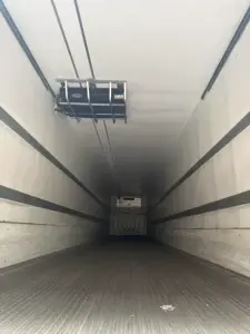 Inside a refrigerated trailer with a load platform near the ceiling and a truck overhang in the distance, showing the long, empty cargo area.