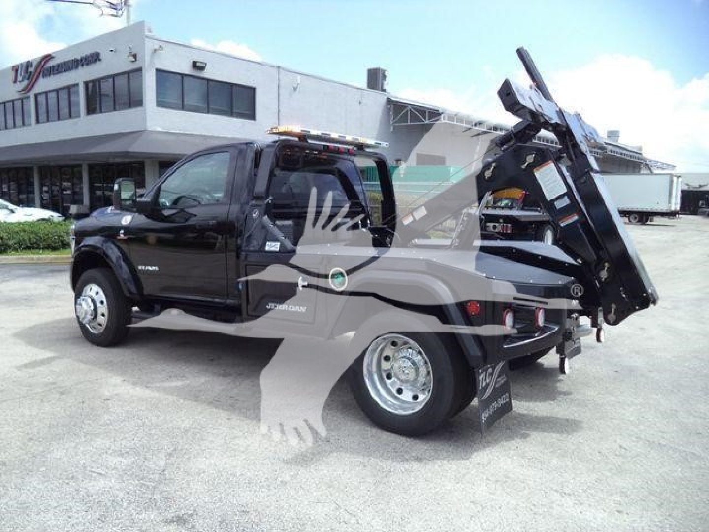 Tow truck with black Ram 4500 chassis, tilt bed/dump style with crane at rear, side badge shows RAM 4500 and Cummins logo, dealership background.