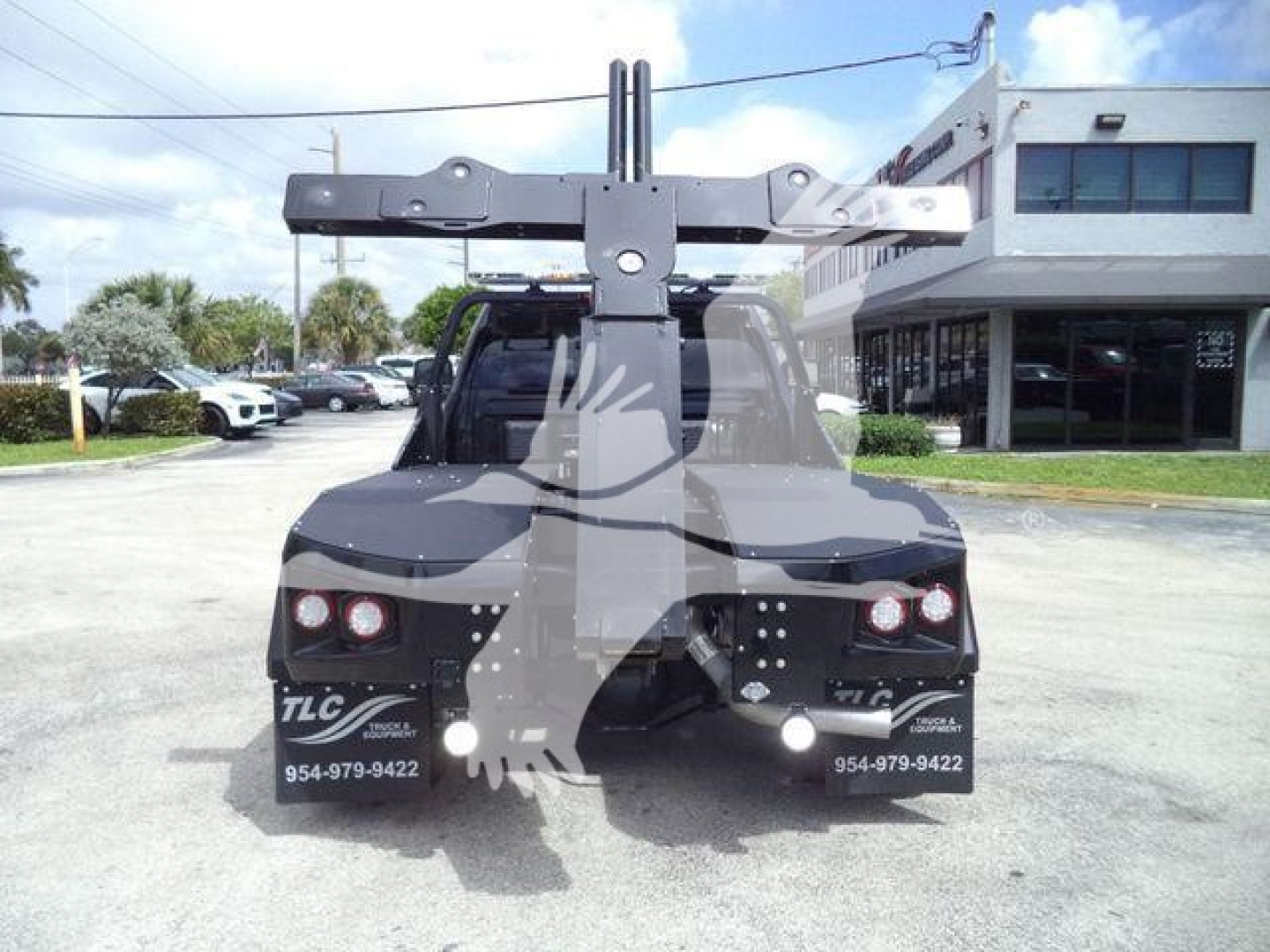 Ram 4500 truck rear view with winch mounting and hitch, visible stickers say TLC and phone numbers, dealership building in background.