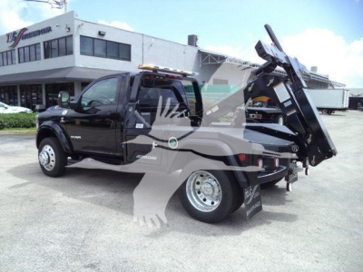 Tow truck with black Ram 4500 chassis, tilt bed/dump style with crane at rear, side badge shows RAM 4500 and Cummins logo, dealership background.