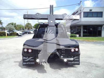 Ram 4500 truck rear view with winch mounting and hitch, visible stickers say TLC and phone numbers, dealership building in background.