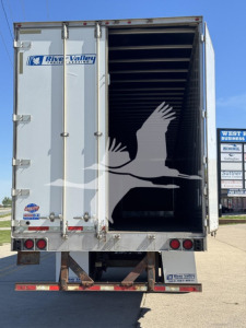 Back view of a silver utility trailer with open rear doors, River Valley trailer sales logo, and an image of a bird graphic inside.