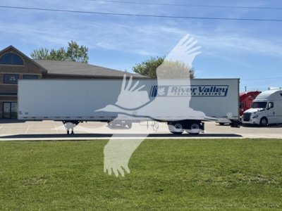 Trailer side view showing a long white utility trailer with River Valley trailer racing logo and text blurred overlay.