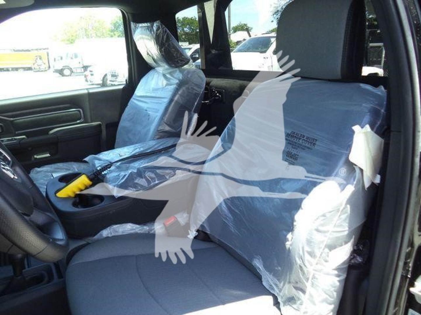 Interior of a new 2024 Ram 4500 SLT pickup showing front seats covered in plastic, steering wheel, center console, and protective wrap.