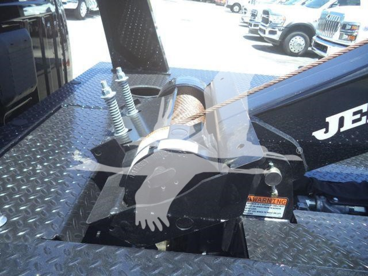 Winch-equipped Ram 4500 pickup truck bed with synthetic winch line and steel hook; visible components include the winch housing, fairlead, mounting frame, and warning label.