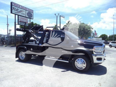 Ram 4500 SLT tow truck/flatbed with winch setup, black and gray cab, chrome wheels, dealership in background.
