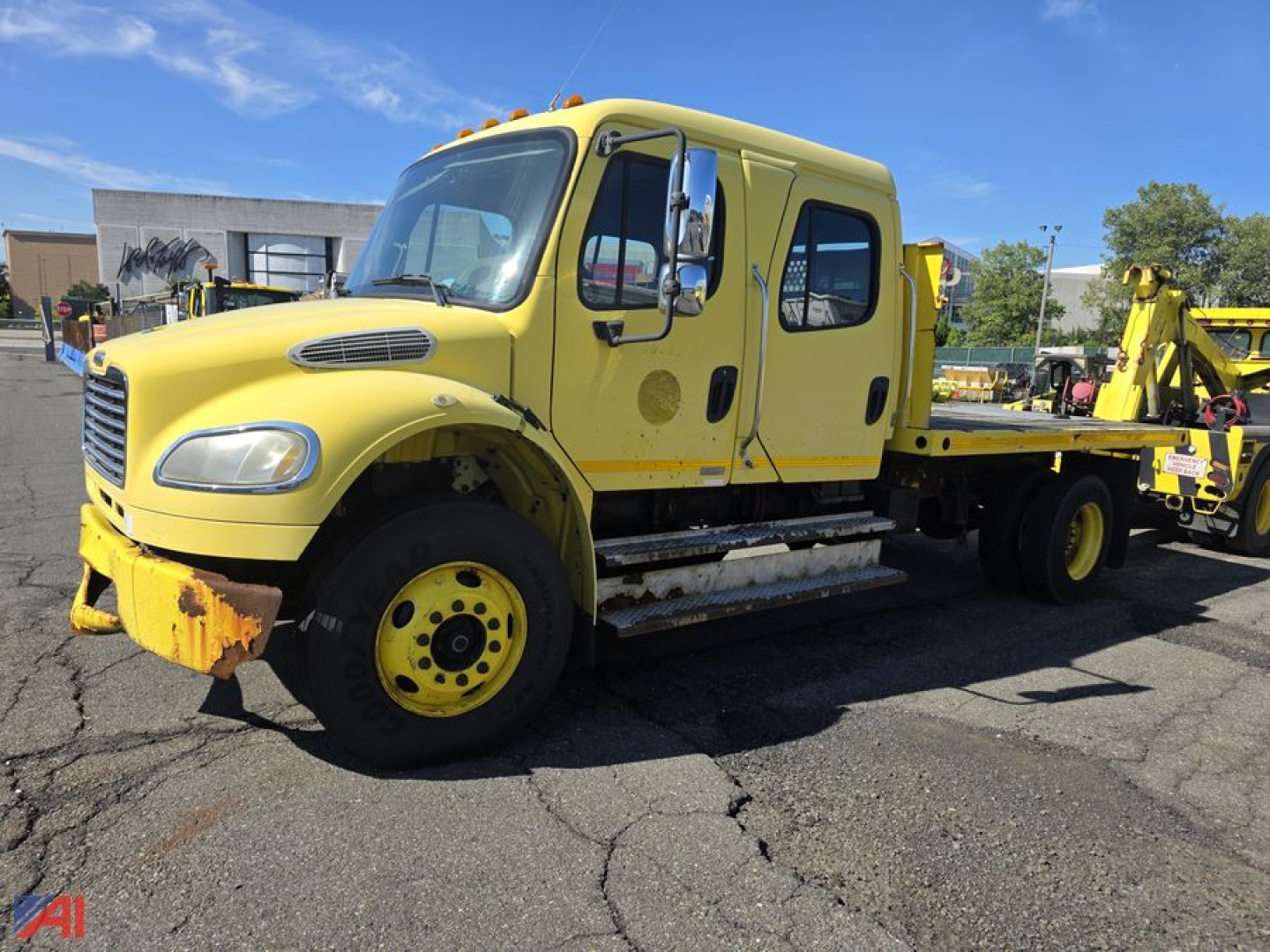 Freightliner M2 106 flatbed truck, yellow, front-left view, dual cab with step rails and flatbed equipment visible.