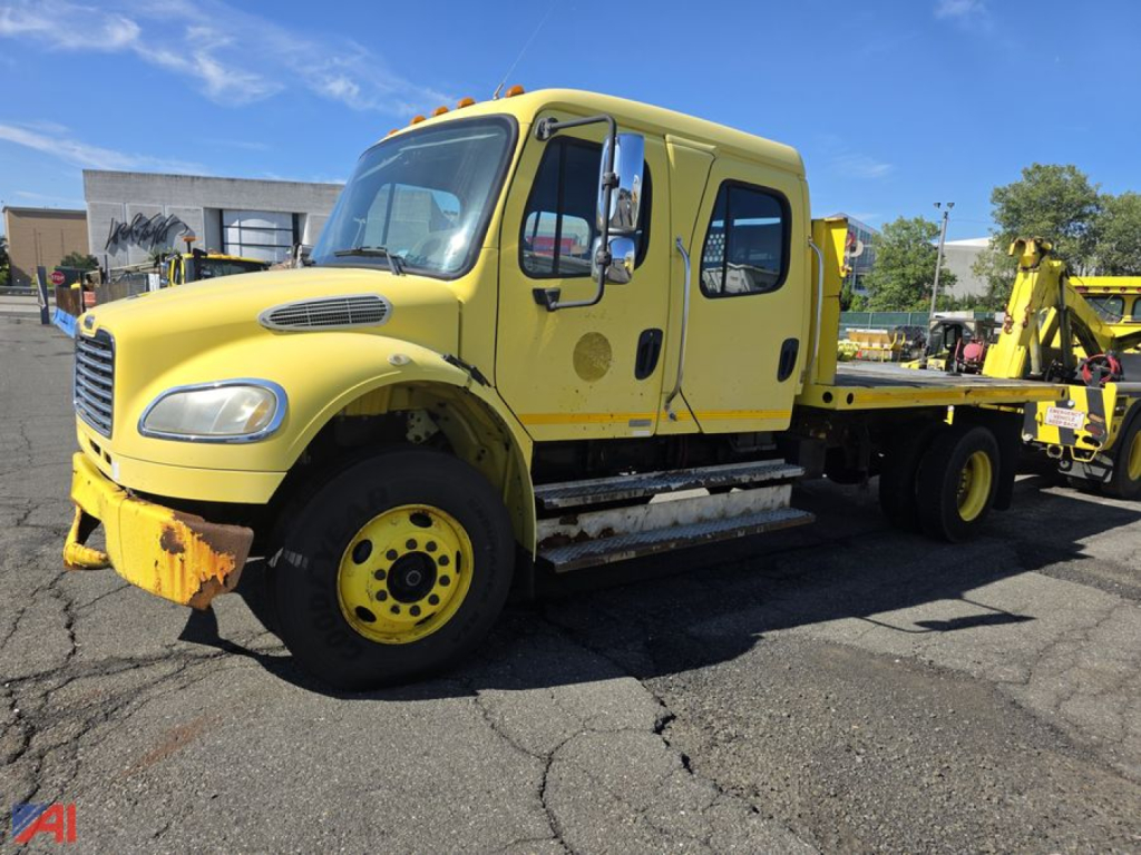Freightliner M2 106 flatbed truck, yellow, front-left view, dual cab with step rails and flatbed equipment visible.