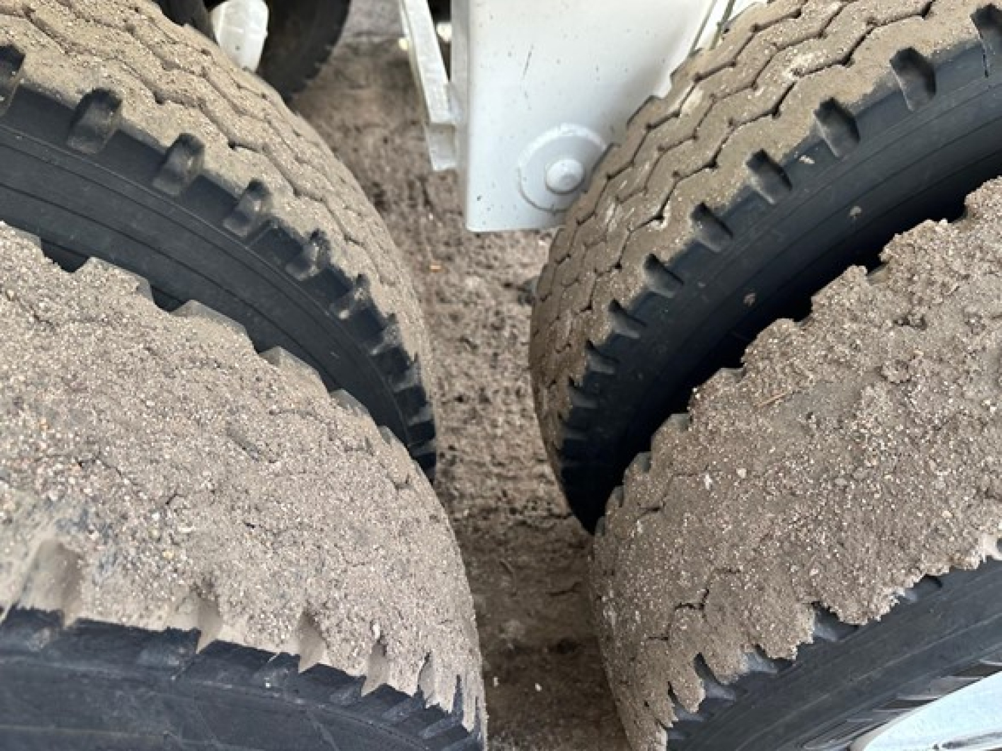 Tires of a dump trailer showing dirt and tread patterns; part of frame and suspension visible.
