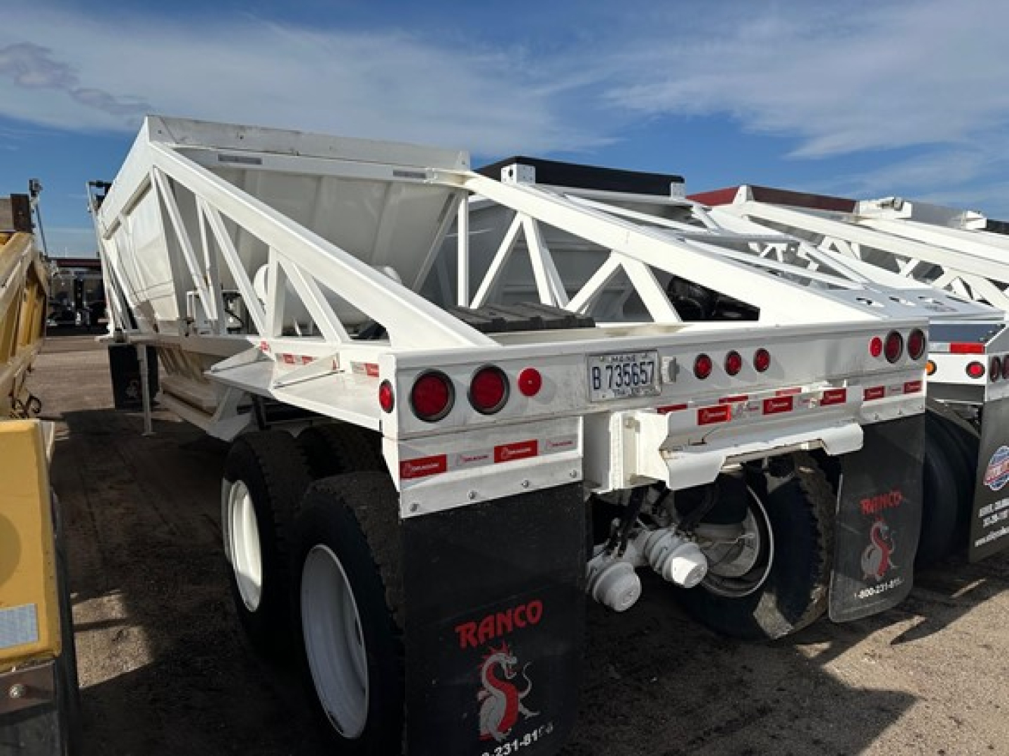 Dump trailer by Ranco Versa with white steel frame and lattice sides, dual rear axles, twin-tire setup, and rear bumper area visible.