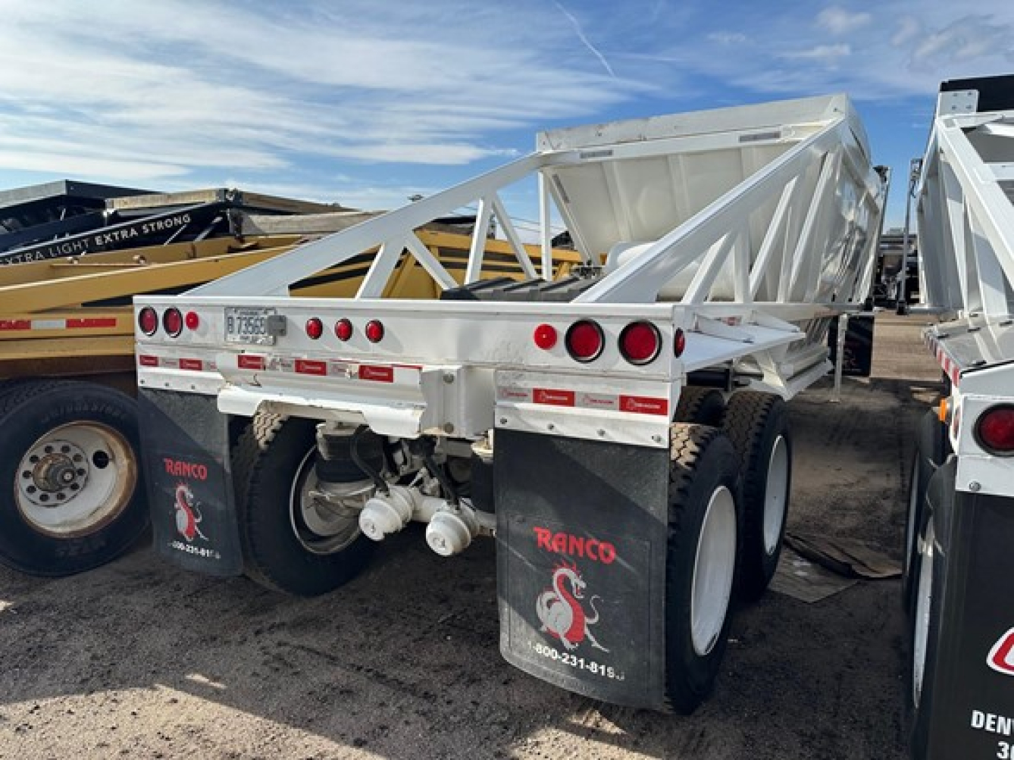 Dump trailer rear view showing tandem axles with white Ranco Versa brand mud flaps and triangle bed frame.