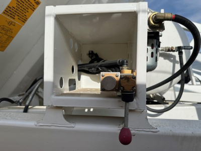 Bottom dump trailer hydraulic control valve and reservoir mount inside a white metal housing on a trailer, with hoses and fittings visible.