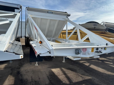 Dump trailer showing Versa Ranco Versa with triangular tri-fold side braces and rear gate, white paint, front hitch, trailer legs, and reflective markings.