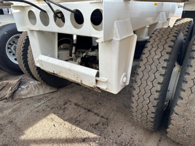 Front lower section of a dump trailer showing dual rear wheels, white painted frame, and hydraulic components.