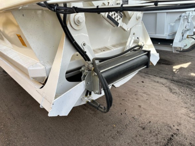 Front lower corner of dump trailer showing hydraulic hose, roller mechanism, and steel frame with a black roller gate; Versa Ranco brand component visible.