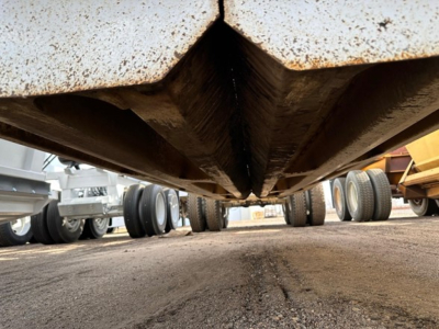 Dump trailer undercarriage view showing rusted underside and wheels in background.