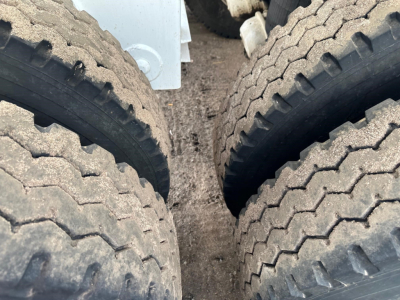 Trailer tires and dual-axle gap with dirt on treads, part of a dump trailer front near the frame components.