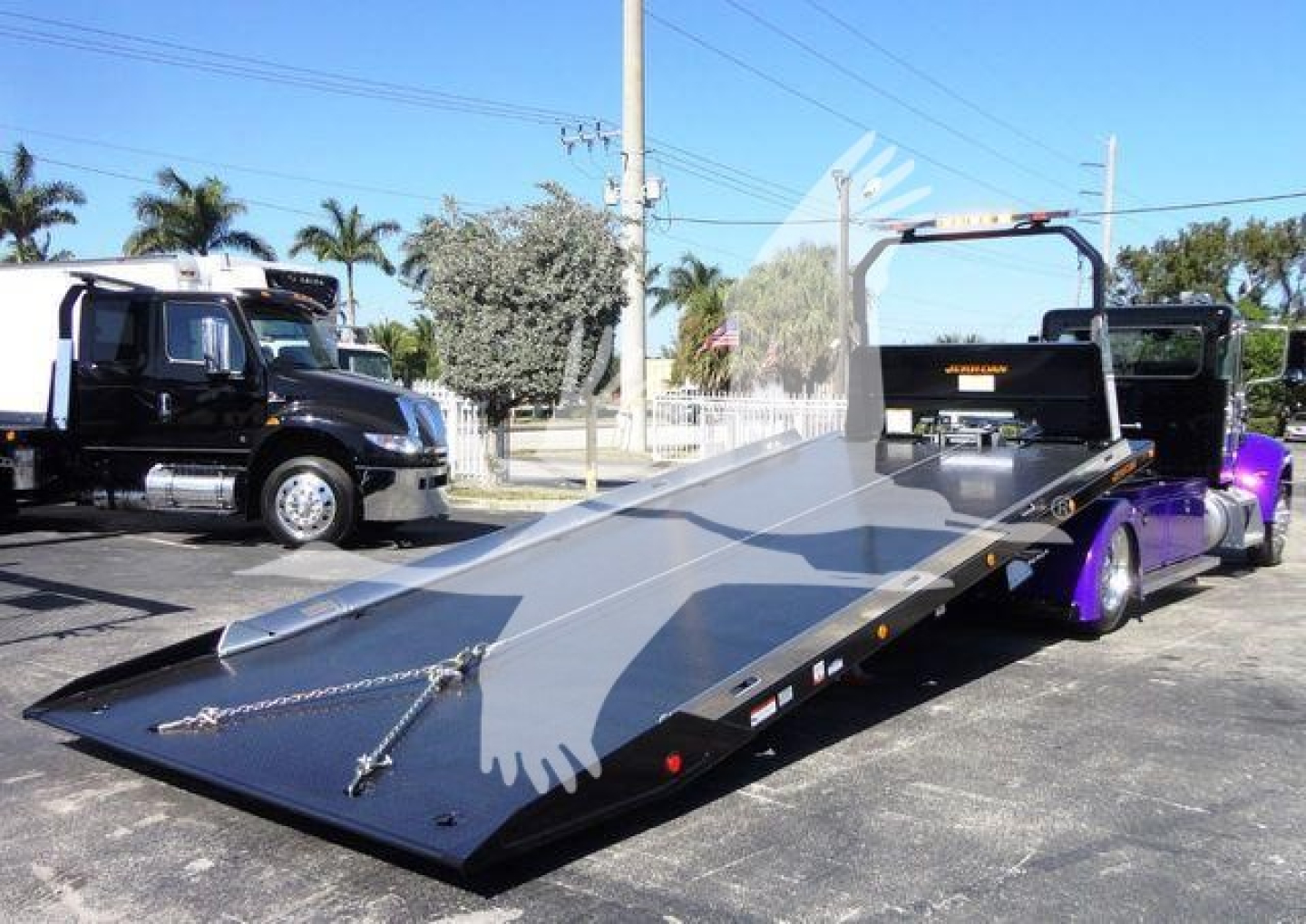 Flatbed tow truck with a black cab and purple accents, low-angle view showing the long metal deck and ramps.