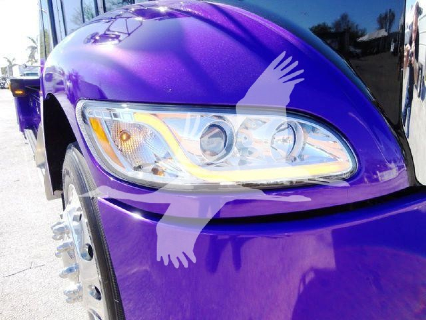 Close-up of a purple 2022 Peterbilt 337 front fender and headlight showing the curved LED daytime running light and chrome headlight housing.