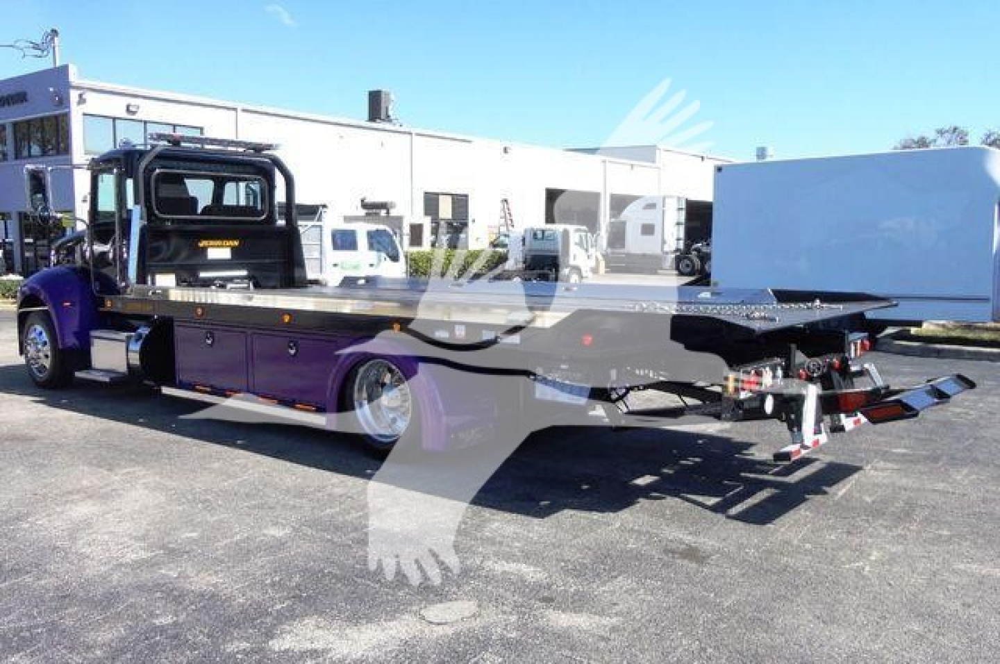 Peterbilt 337 rollback truck with purple cab and flatbed, side toolbox compartments, and hydraulic rollback mechanism visible at rear.