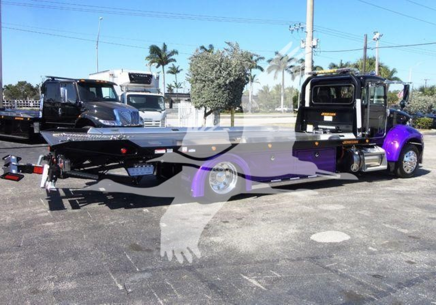 Peterbilt 337 rollback tow truck in a parking lot, long flatbed with purple accents, black cab, rear hitch and tow setup visible.