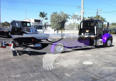 Peterbilt 337 rollback tow truck in a parking lot, long flatbed with purple accents, black cab, rear hitch and tow setup visible.