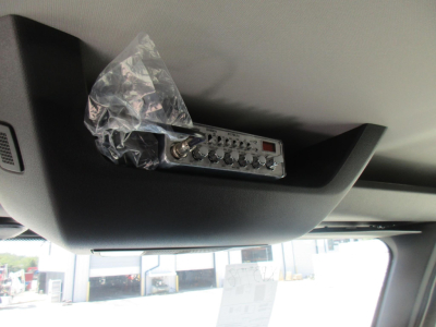 Overhead sun visor area with a wired control module mounted, plastic bag over it, dashboard window visible; control panel shows multiple dial knobs and a small display.
