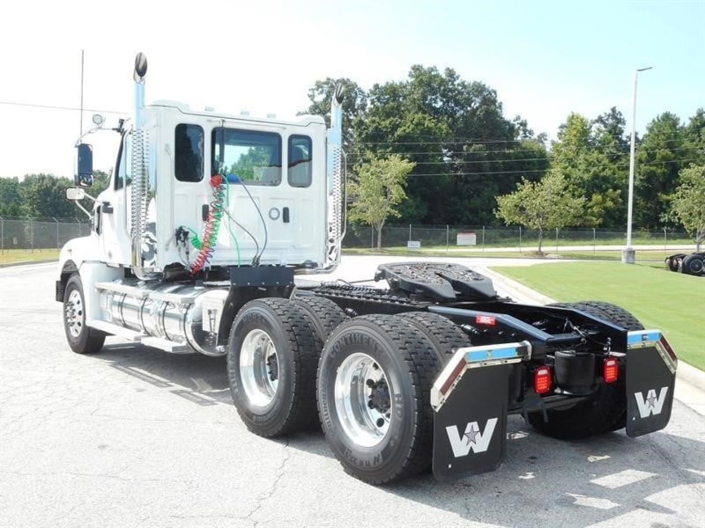 Western Star 49X day cab tractor from rear-left angle showing dual rear axles and fifth-wheel, chrome exhaust stacks, and Mudflaps with W logo.