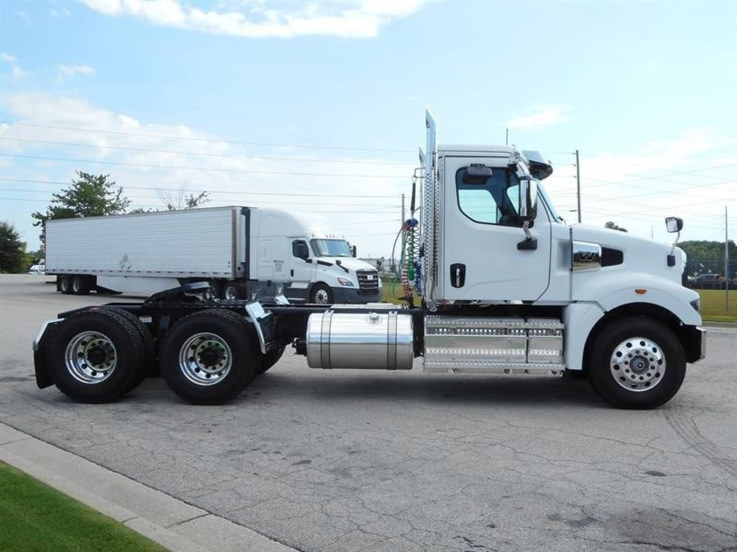 Semi truck side view showing Western Star 49X with white cab and dual rear axles, day cab configuration, chrome fuel tanks and steps.