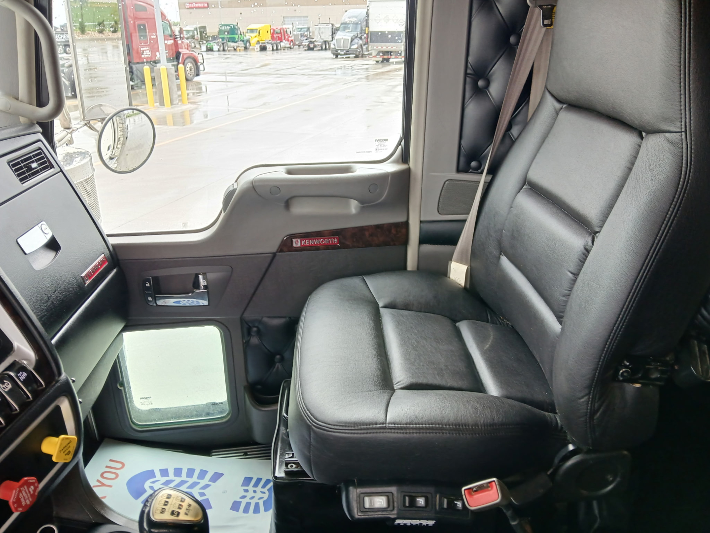 Kennworth W900L cab interior showing leather driver seat and dashboard. Window view shows truck yard.