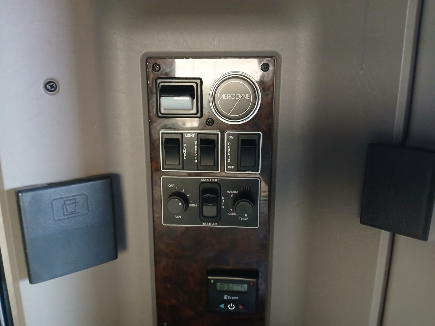 Dashboard/control panel with multiple switches and a circular ident badge reading AROFY? or typical truck controls, and a digital gauge; surrounding panel has a woodgrain finish.