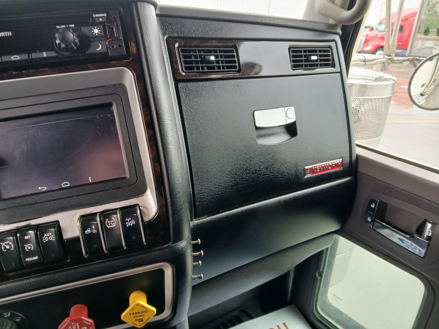 Kenworth W900L truck interior dashboard view showing center console with touchscreen display, knobs, vents, glove box, and side door panel.