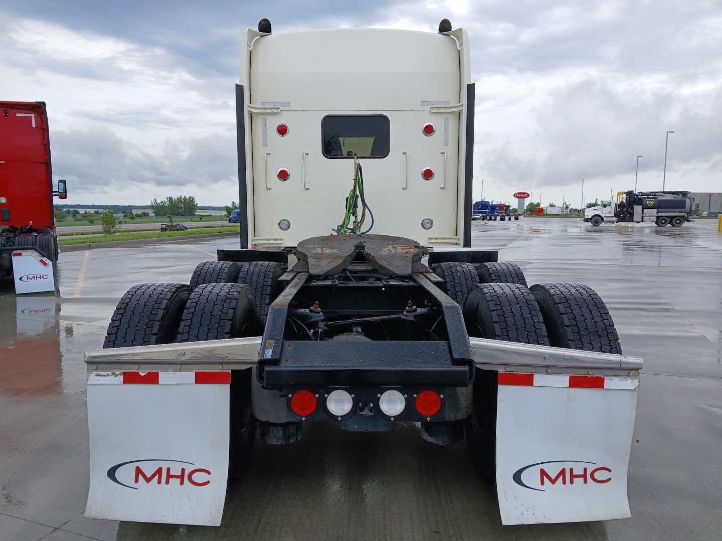Kenworth W900L rear view showing fifth wheel, dual rear axles, and mud flaps with MHC logo.
