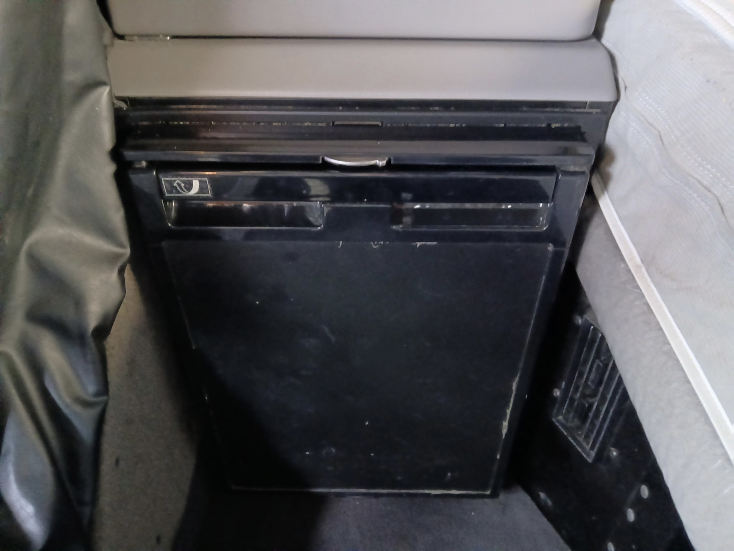 Conventional sleeper truck interior showing a small black refrigerator/freezer unit mounted under a shelf.