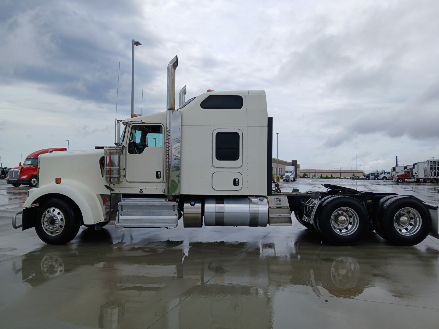 Side view of a white Kenworth W900L semi-truck with sleeper cab and chrome exhaust stacks.