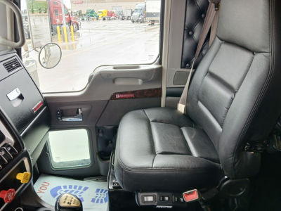 Kennworth W900L cab interior showing leather driver seat and dashboard. Window view shows truck yard.