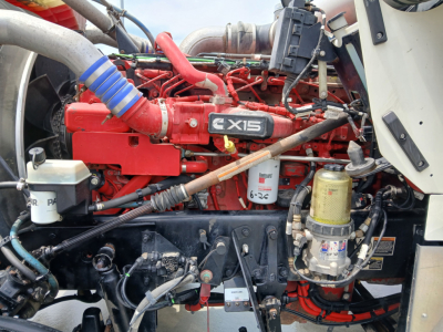 Kenworth W900L engine bay with a red Cummins X15 engine and various hoses, filters, and components visible.