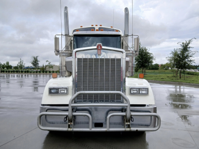 Kenworth W900L truck front view with tall exhaust stacks and chrome grille guard in a wet lot.