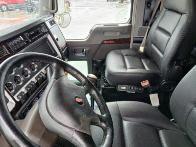 Kenworth W900L interior showing steering wheel, dashboard with gauges, driver seat, and center console; black leather seats; door panel with wood trim.