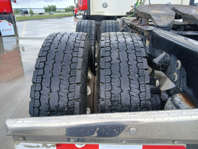 Kenworth W900L truck rear dual tires with tread pattern visible on wet concrete, metal frame and chassis nearby.