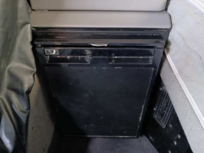 Conventional sleeper truck interior showing a small black refrigerator/freezer unit mounted under a shelf.