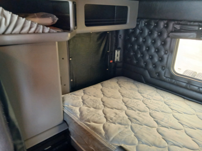 Kenworth W900L sleeper cab interior with queen-size bed and tufted black leather panels.