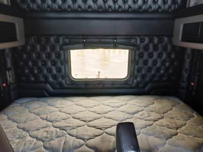 Interior sleeper cab of a Kenworth W900L showing a padded black quilted wall, window, and a fitted mattress.