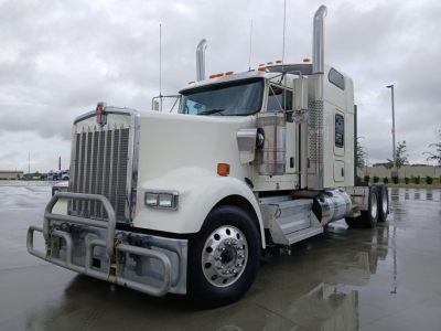 Kenworth W900L truck cab and front sleeper with chrome grille guard and dual exhaust stacks, white paint, on a wet lot.