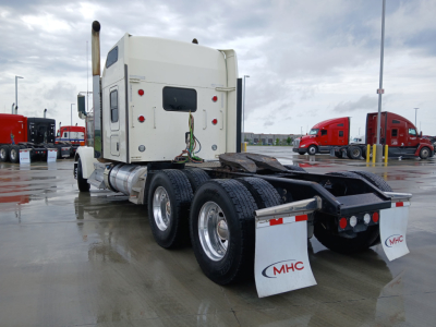 Kenworth W900L truck in a dealership lot, rear view showing sleeper cab, twin rear axles, fuel tanks, and mudflaps with CMHC logos.