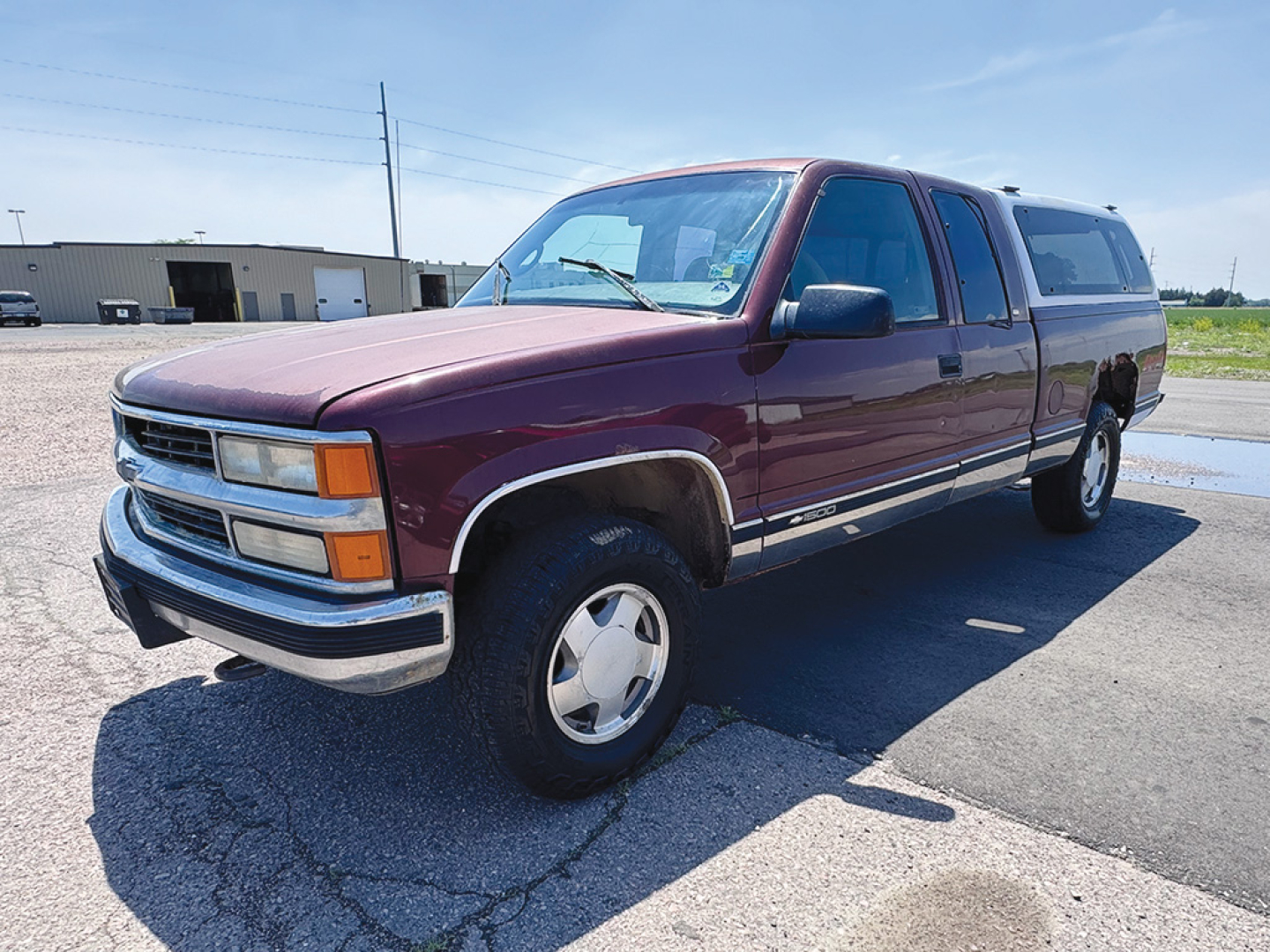 Chevrolet Silverado extended cab 4x4 pickup in maroon with camper shell, front driver side view showing chrome bumper and wheel, early 2000s style.