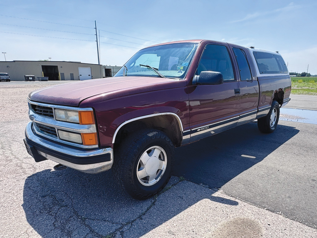 Chevrolet Silverado extended cab 4x4 pickup in maroon with camper shell, front driver side view showing chrome bumper and wheel, early 2000s style.