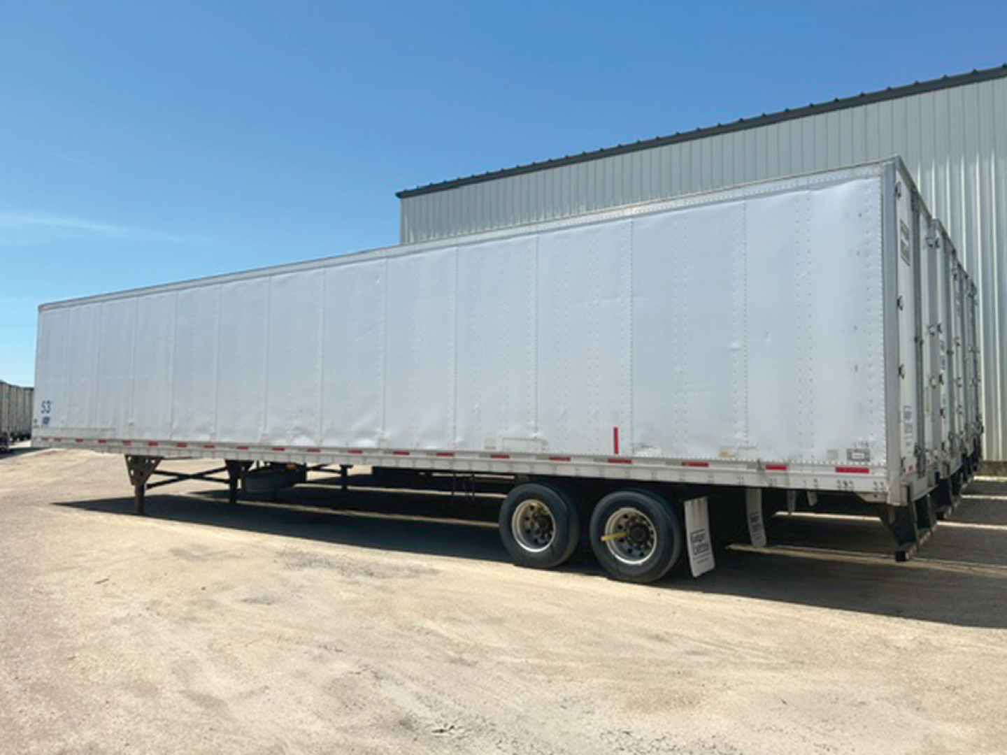 Utility trailer showing tandem axle setup and long rectangular cargo trailer with white corrugated sides.