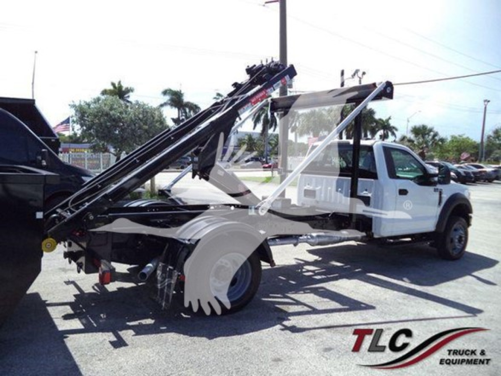 Ford F-550 rolloff truck showing hydraulic arms and bed in serviceable condition with white cab and black equipment, rear view angled to left.